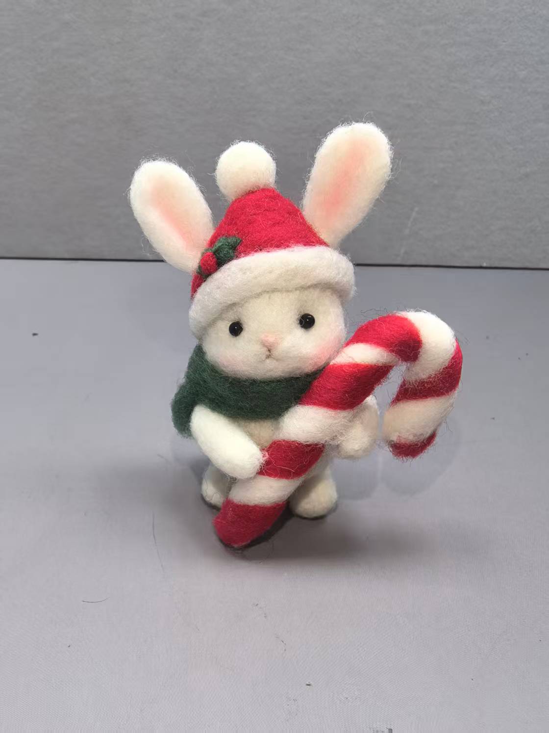 Needle felted white bunny in a Santa hat and green scarf hugging a striped candy cane