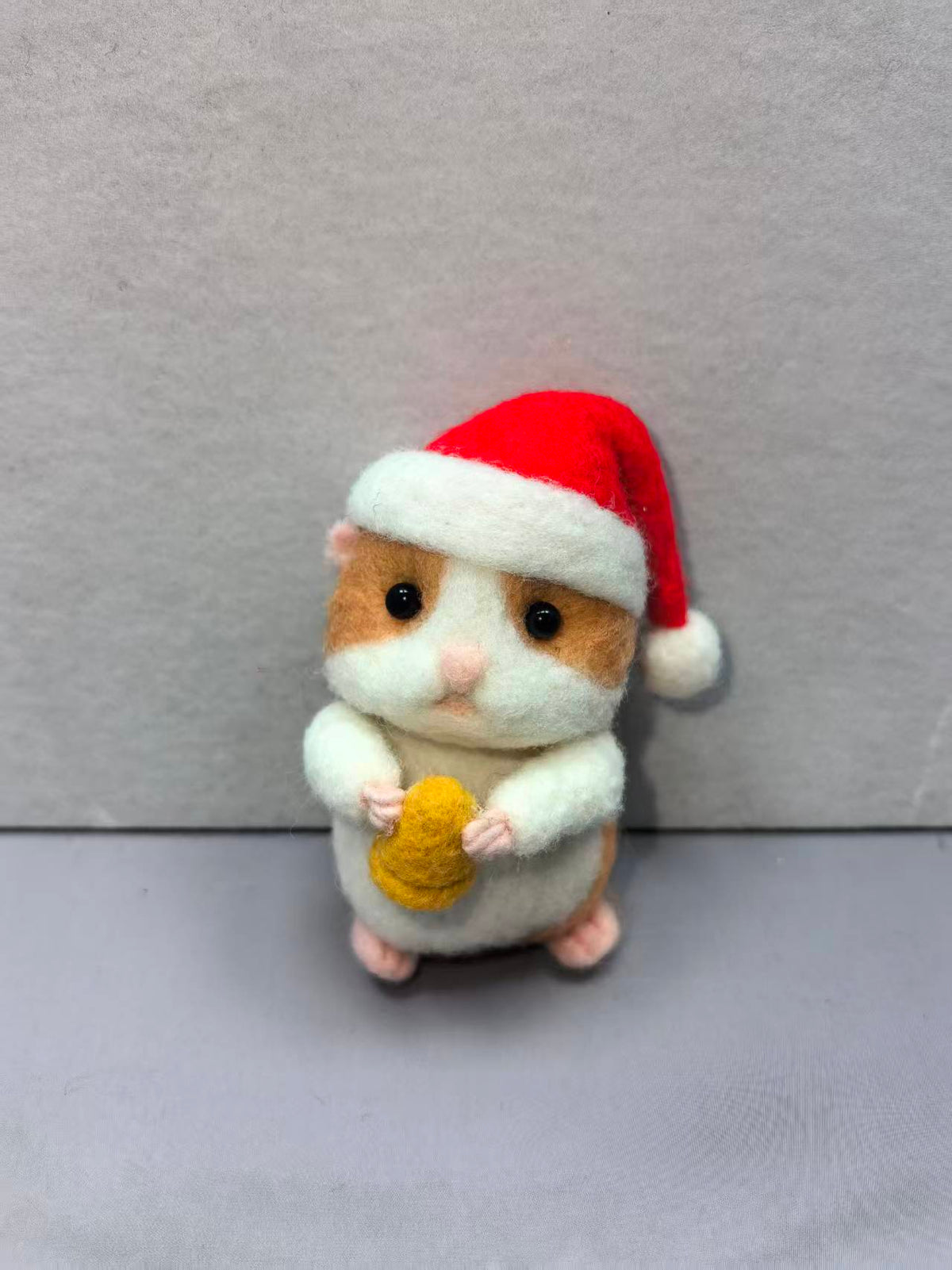 Needle felted hamster in a red Santa hat holding a treat