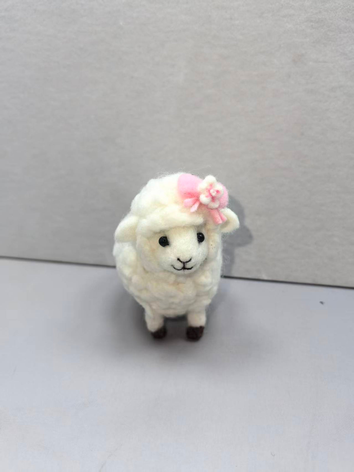 Needle felted curly white sheep wearing a pink hat with a flower